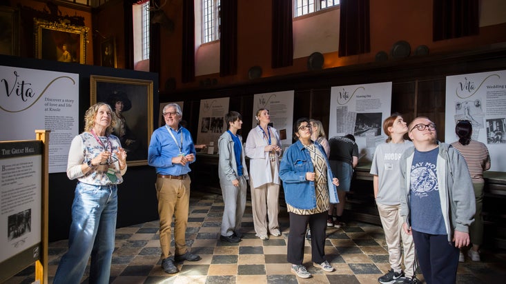 A group of male and female people in a large room that has a black and white tiled floor and exhibition panels saying Vita in the background